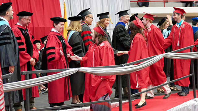 photo graduating students walking across a stage and shaking hands with professors