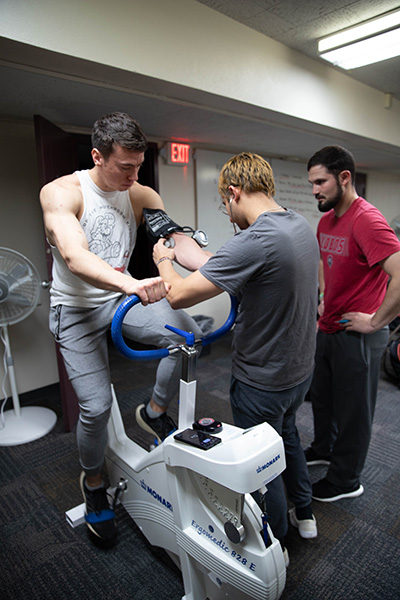 male student taking blood pressure of male student on exercise bike