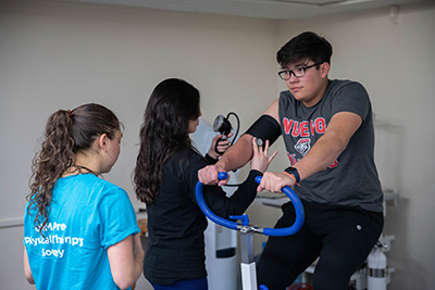 a male student riding an exercise bike while a female student checks vital signs