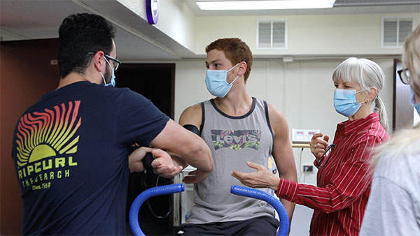 photo of a students and an instructor taking medical readings from a student on a stationary bike
