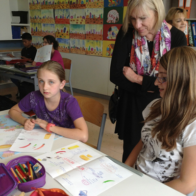 Deborah Rifenbary, UNM College of Education associate dean and  coordinator of the STARS program, looks over the shoulder of  Austrian schoolchildren as they create posters depicting New Mexico.