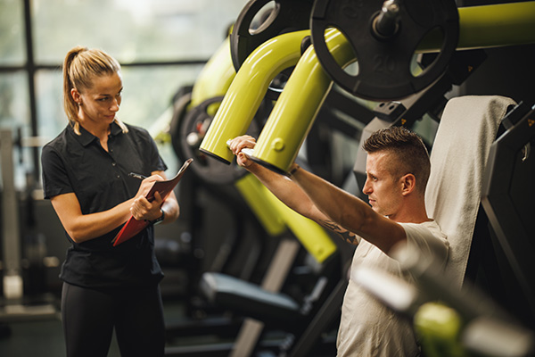 photo of a woman coaching a man who is using upper body weightlifting equipment