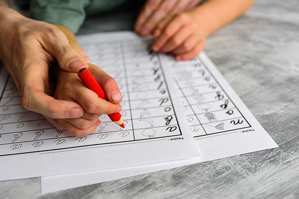 adult hand holding child's hand guiding the child as it practices writing ABCs